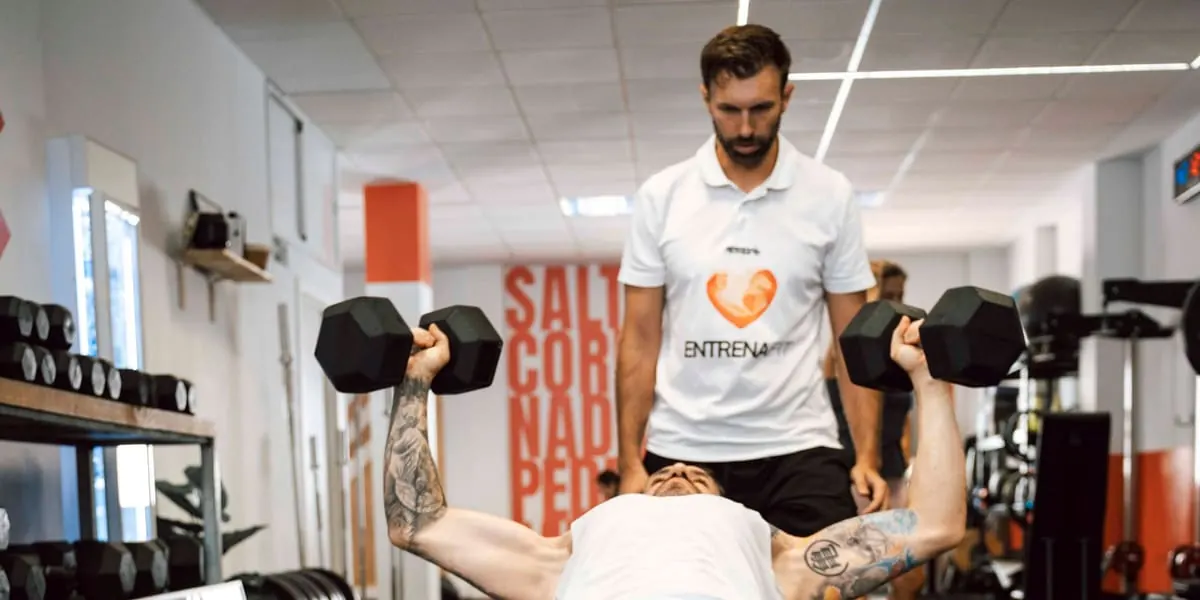 Entrenador supervisando un press con mancuernas en el gimnasio Entrenafit de Las Lagunas de Mijas