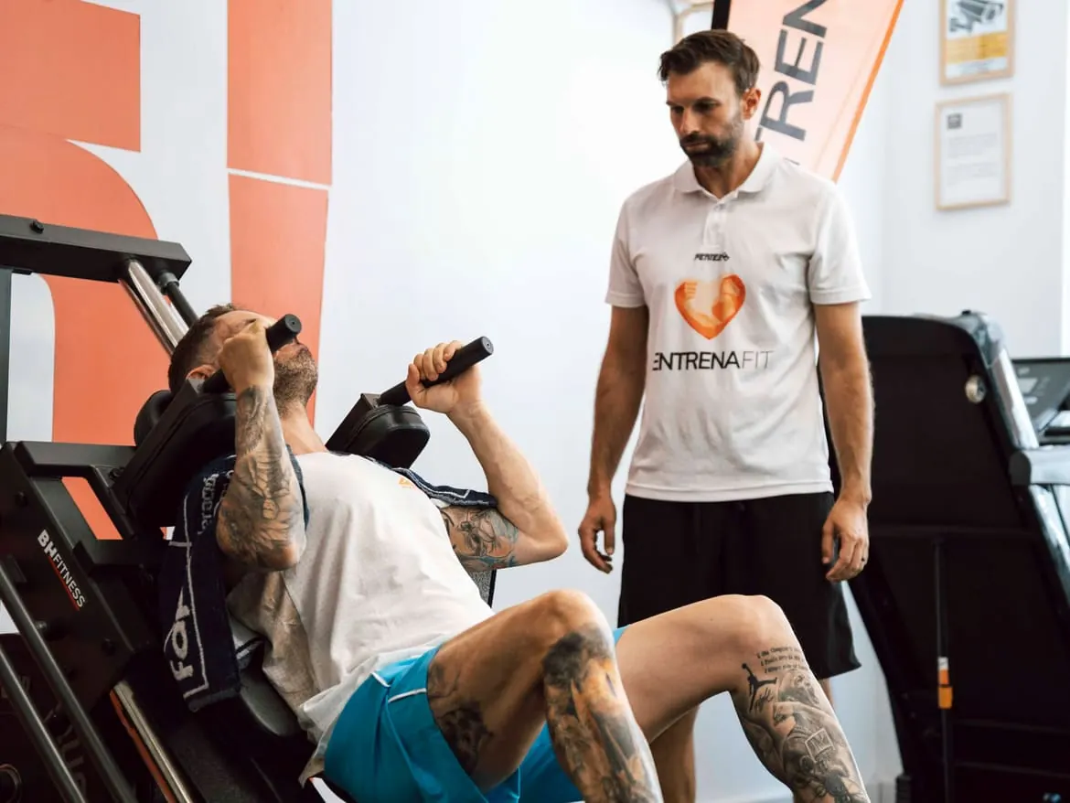 Entrenador supervisando un ejercicio en prensa de piernas en Entrenafit, Las Lagunas de Mijas